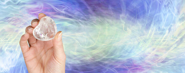 Crystal healer holding clear quartz puff heart gem stone - female hand offering a large heart shaped crystal  against a green blue purple energy formation  background with copy space