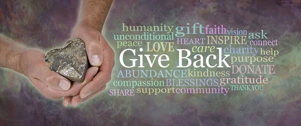 Give Back from the Heart Word Cloud - male hands gently cupped around a wooden heart beside a  GIVE BACK word tag cloud against a wide rustic dark multicoloured grunge background