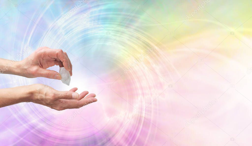 Crystal Healer using clear quartz terminate wand - Female hand pointing a clear quartz terminated crystal into palm of hand against a rainbow coloured spiraling  vortex background with copy space on right