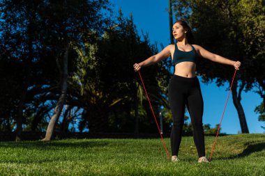 Güzel beyaz bir kadın parkta lastik bantla spor yapıyor.