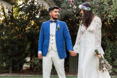 Mutlu ve güzel yeni evliler el ele yürüyorlar ve birbirlerine sevgiyle bakıyorlar.