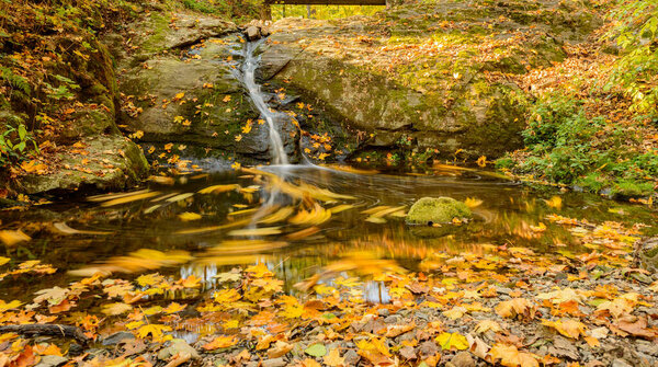 smaller waterfall over rock with fallen colored leaves in autumn, long exposure, stribro
