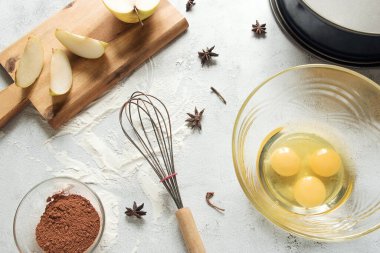 Cam kasede yumurtalar, çırpı, kakao tozu, turta tabağı, yıldız anason kabukları ve elma dilimleri.
