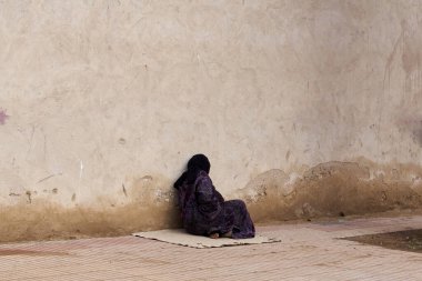 Peçeli yaşlı kadın geleneksel giysiler içinde Fas duvarında tek başına oturuyor.                               