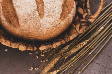 Hasır sepette taze ekmek ve masada buğday başakları.