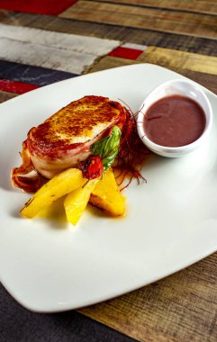 Domuz pastırması, patates ve sosla sarılmış ahşap bir masada beyaz bir tabakta.