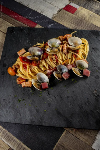 İstiridye ve ton balıklı spagetti. Tahta bir masada siyah bir levha.