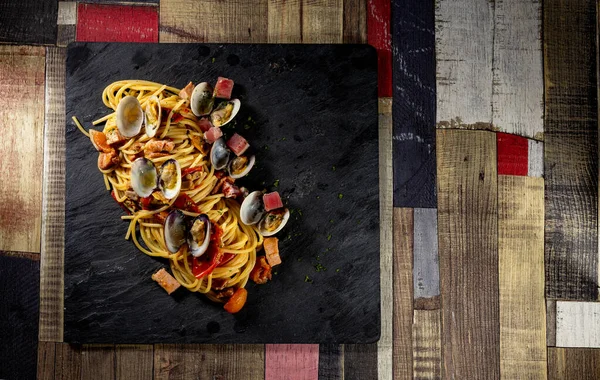 İstiridye ve ton balıklı spagetti. Tahta bir masada siyah bir levha.