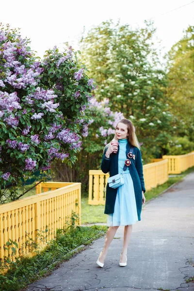 Mujer atractiva está caminando al aire libre en primavera. Arbusto lila delante de la chica . —  Fotos de Stock