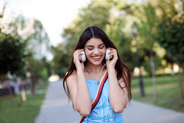 Glücklich lächelnde Frau hört draußen im Park Musik in ihren Kopfhörern. — Stockfoto