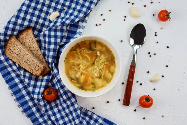 Вкусный суп с лапшой и картошкой, кусочки хлеба на белом столе . — стоковое фото