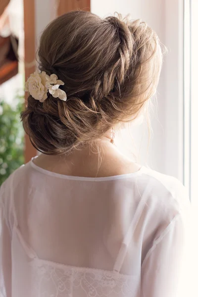 Mañana hermosa joven feliz de la novia cerca de una ventana en un vestido blanco con un hermoso boudoir peinado festivo noche con adornos en el pelo y maquillaje suave — Foto de Stock