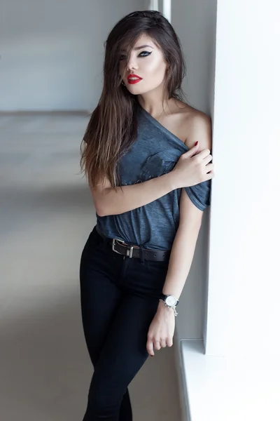 Όμορφη σέξι κορίτσι με μακριά σκούρα μαλλιά στυλ κουνιστή πολυθρόνα με κόκκινο κραγιόν για gubyh μόνιμη κοντά σε ένα παράθυρο σε ένα μαύρο δερμάτινο μπουφάν — Φωτογραφία Αρχείου