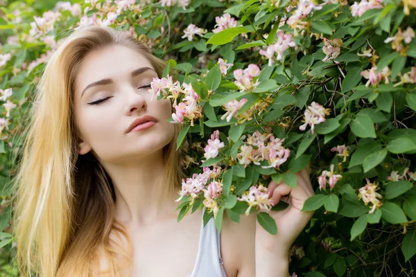 Vackra vackra flicka med långa blonda hår njuter av naturen nära blommande rosenbuske i en vit t-shirt med fylliga läppar ljusa sommardag — Stockfoto