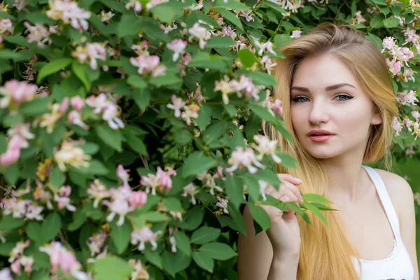 Hermosa chica encantadora con el pelo largo y rubio disfrutando de la naturaleza cerca de la floración de rosal en una camiseta blanca con los labios llenos brillante día de verano —  Fotos de Stock