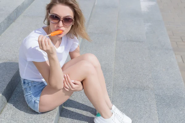 Красивая молодая сексуальная девушка сидит на лестнице в шортах и солнцезащитных очках и ест вкусное мороженое ярко — стоковое фото