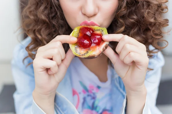 Schöne sexy Mädchen mit dunklem lockigem Haar, essen einen hellen saftigen Obstkuchen mit einem großen Appetit — Stockfoto