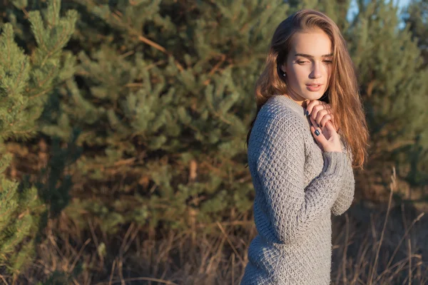 Beautiful lonely young girl with big eyes and wide bushy eyebrows in a warm sweater walking in the forest at sunset — Stock Photo, Image