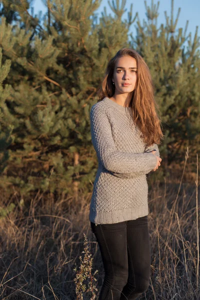 Beautiful lonely young girl with big eyes and wide bushy eyebrows in a warm sweater walking in the forest at sunset — Stock Photo, Image