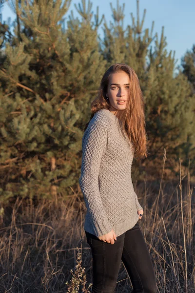 Beautiful lonely young girl with big eyes and wide bushy eyebrows in a warm sweater walking in the forest at sunset — Stock Photo, Image