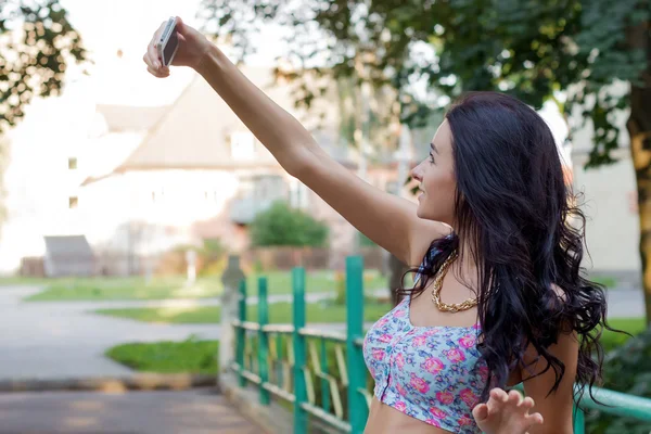 Bella giovane donna bruna con i capelli scuri in piedi con il telefono invia messaggi SMS e fa selfie — Foto Stock