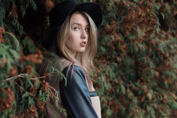 Lonely sad pretty cute blond girl with blue eyes and full lips in black hat and coat walking in autumn forest — Stock Photo, Image