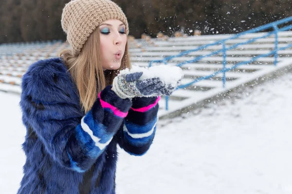 Mooi helder vrolijk meisje met blauwe vacht spelen in de sneeuw — Stockfoto