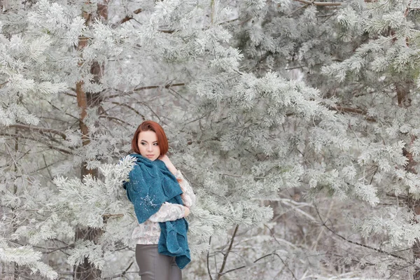 Belle fille aux cheveux roux avec une écharpe sur les épaules marchant dans la forêt hivernale de sapins et de pins étouffés — Photo