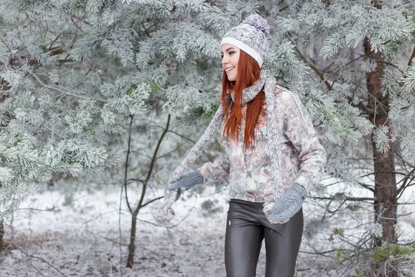 Mooie vrolijke gelukkig meisje met rood haar in een warme muts en sjaal spelen en gek rond in de sneeuw in de winter forest — Stockfoto