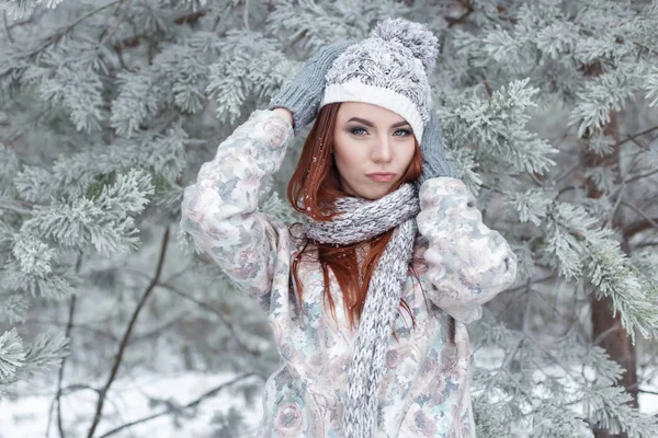 Mooie vrolijke leuk roodharige meisje in een cap en sjaal speelt met sneeuw in de prachtige forest fairy — Stockfoto