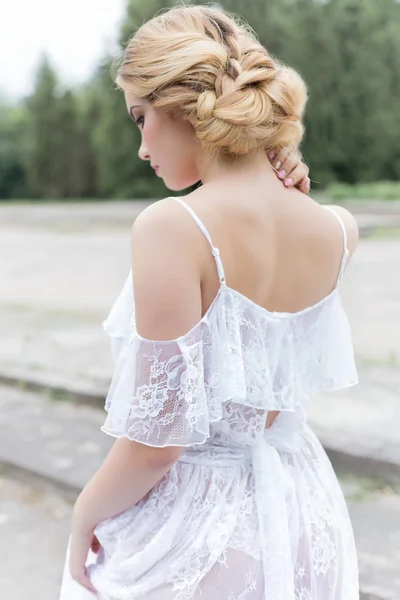 美丽年轻的甜金发碧眼的女孩，在手中的白裙与晚宴发型闺房的婚礼花束走在废墟附近 — 图库照片