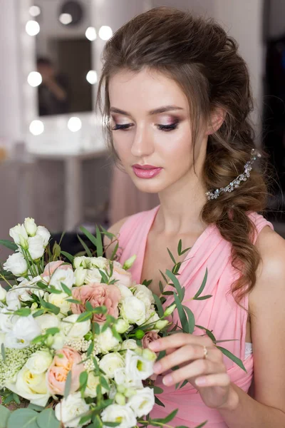 Schöne süße Mädchen Brautjungfer bereitet sich auf die Hochzeit eines Freundes im rosa Abendkleid mit Abendfrisur und helles Make-up mit einem Strauß der Hände der Braut — Stockfoto