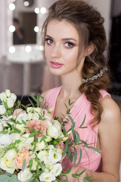 Bela dama de honra menina doce se preparando para o casamento de um amigo no vestido de noite rosa com penteado da noite e maquiagem brilhante com um buquê de mãos de noiva — Fotografia de Stock