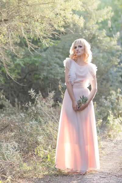 Милая красивая девушка блондинка кудрявые волосы прогулки в лесу в свадебном платье на солнце на закате — стоковое фото