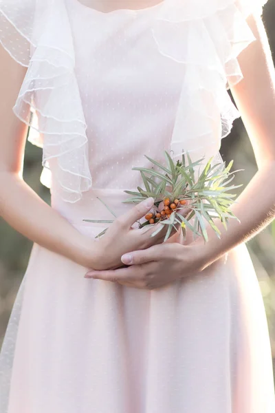 gentle graceful hands of a bride Girl with a branch of sea buckthorn in the hand in a gentle air wedding dress in the sun rays at sunset