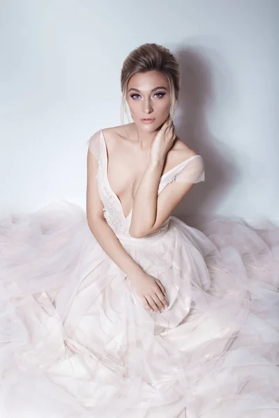 Mooie gevoelige bruid sexy meisje in zachte roze skazachno trouwjurk met een snee in de borst en terug met make-up en kapsel van de avond in de studio op een witte achtergrond — Stockfoto