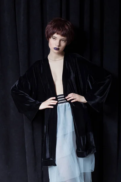 Fashion shot of a beautiful young girl with a cheeky short hair style hipster in black velvet jacket in a studio on a black background — Stock Photo, Image