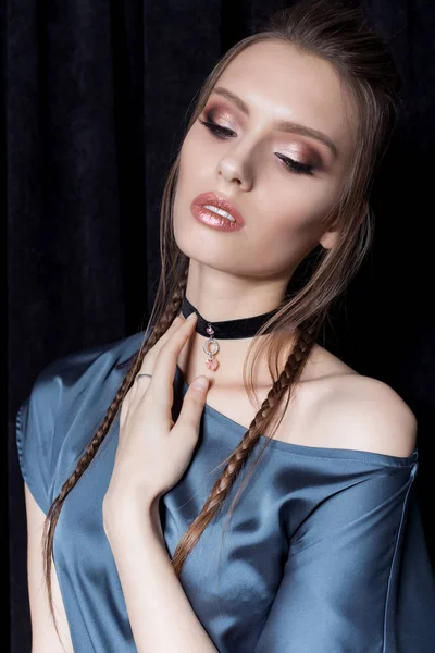 Beautiful sexy young woman with dark hair braided with bright makeup and fashion jewelry choker around her neck, fashion jewelry shooting on a black background in the studio, hard light — Stock Photo, Image