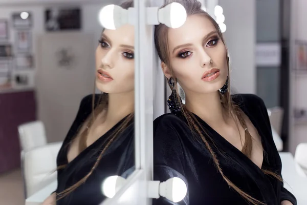 Beautiful sexy girl with hair in the style of rock stands near the mirror in the dressing room in a black velvet gown with a bright spectacular evening jewelry with kriskalami sergt and ring — Stock Photo, Image