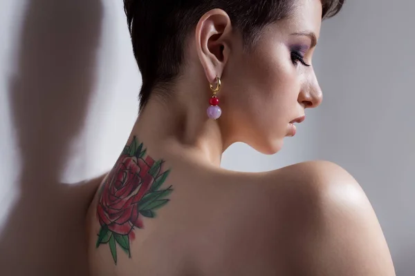 Mooie jonge sexy meisje met kort haar met tatoeage op zijn rug is tegen de muur met blote schouders verdrietig — Stockfoto