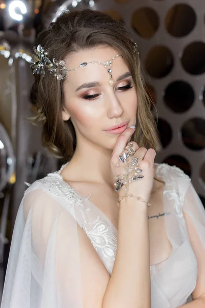 Retrato suave de una hermosa novia feliz lindo con un hermoso peinado festivo maquillaje brillante en un vestido de novia con pendientes y un anillo con un adorno en su cabello —  Fotos de Stock