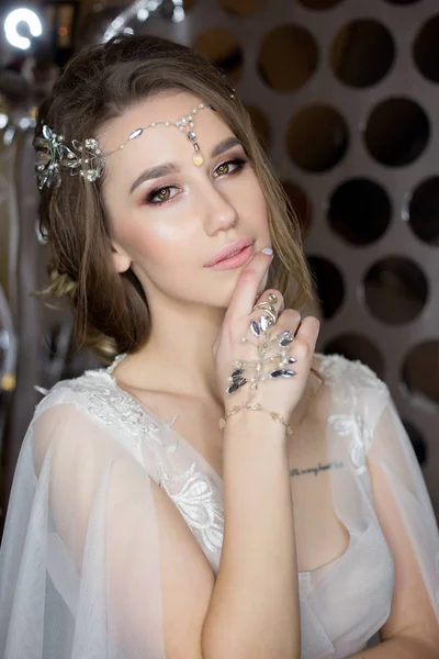 Ritratto gentile di una bella sposa felice carina con una bella acconciatura festiva trucco luminoso in un abito da sposa con orecchini e un anello con un ornamento nei capelli — Foto Stock