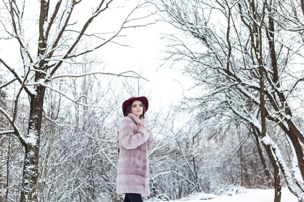 Belle fille élégante mignonne dans un manteau de fourrure et chapeau de marche dans la forêt d'hiver matin givré lumineux — Photo