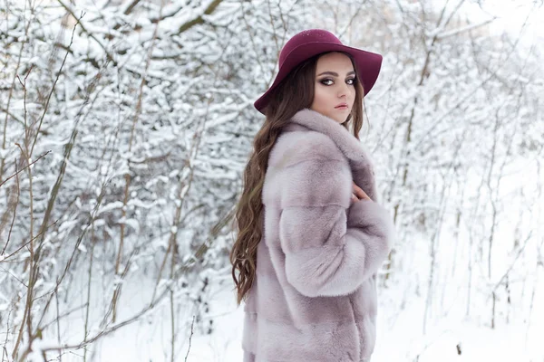 Mooi leuk elegant meisje in een bontjas en hoed wandelen in het bos heldere frosty winterochtend — Stockfoto