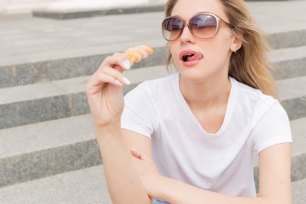 Beautiful young sexy girl in sunglasses eating ice cream on the ladder and licking plump lips a bright sunny hot day