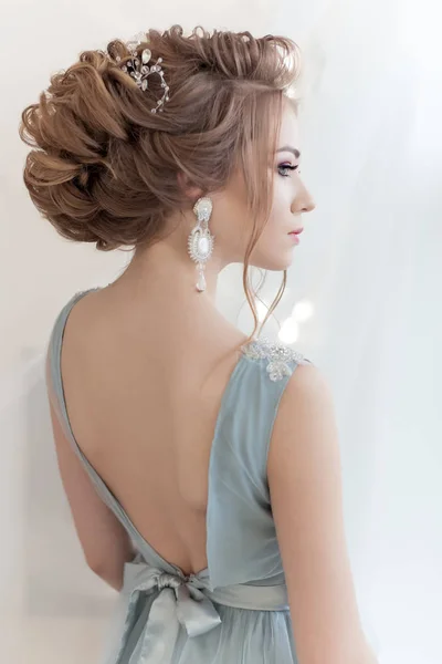 Schöne Volumenfrisur für eine Braut in einem sanften blauen Lichterkleid mit großen Ohrringen und Haarschmuck — Stockfoto