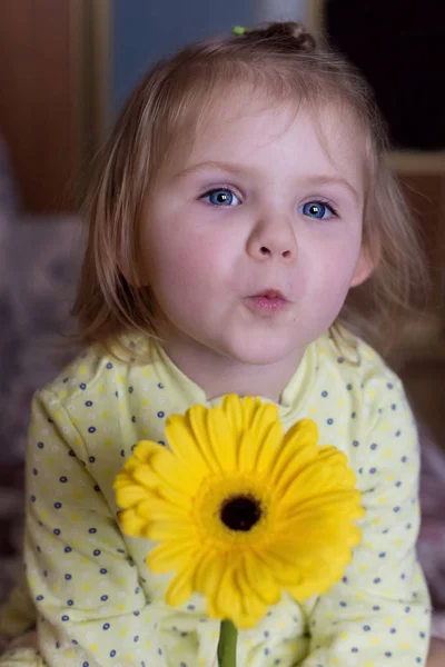 Beautiful little cute girl in a yellow robe sending a kiss to the camera with a yellow daisy flower — Stock Photo, Image