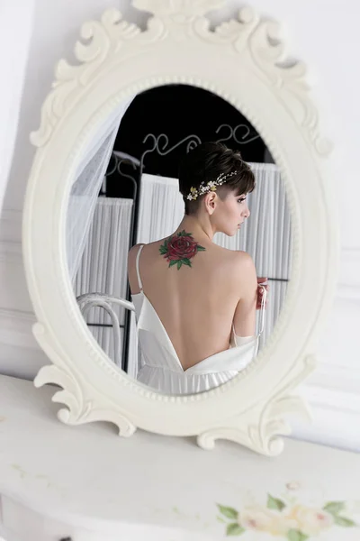 Belle jeune mariée sexuelle tendre avec une coupe de cheveux courte couronne douce sur sa tête avec un tatouage sur le dos dans le linge près du miroir — Photo