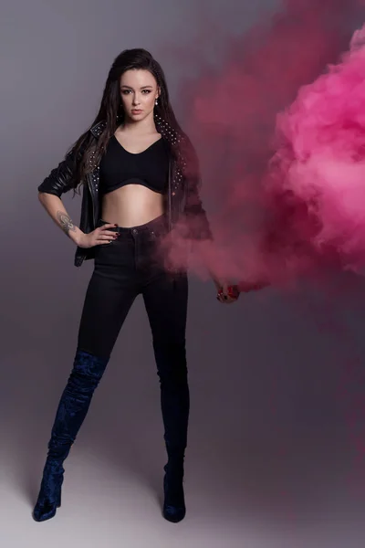 Mooi sexy modieus meisje in zwarte kleding in een coolshot in de studio met gekleurde roze rook — Stockfoto