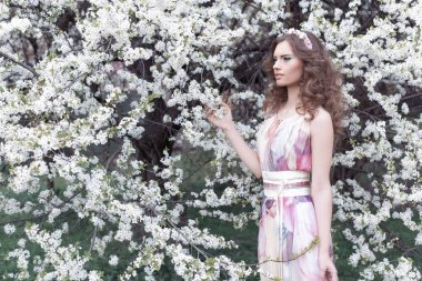 Güzel genç kız ile bukleler bir havada renkli elbise bir çelenk ile kafasındaki bir kiraz çiçeği Parkı güneşli bir günde yürüyüş